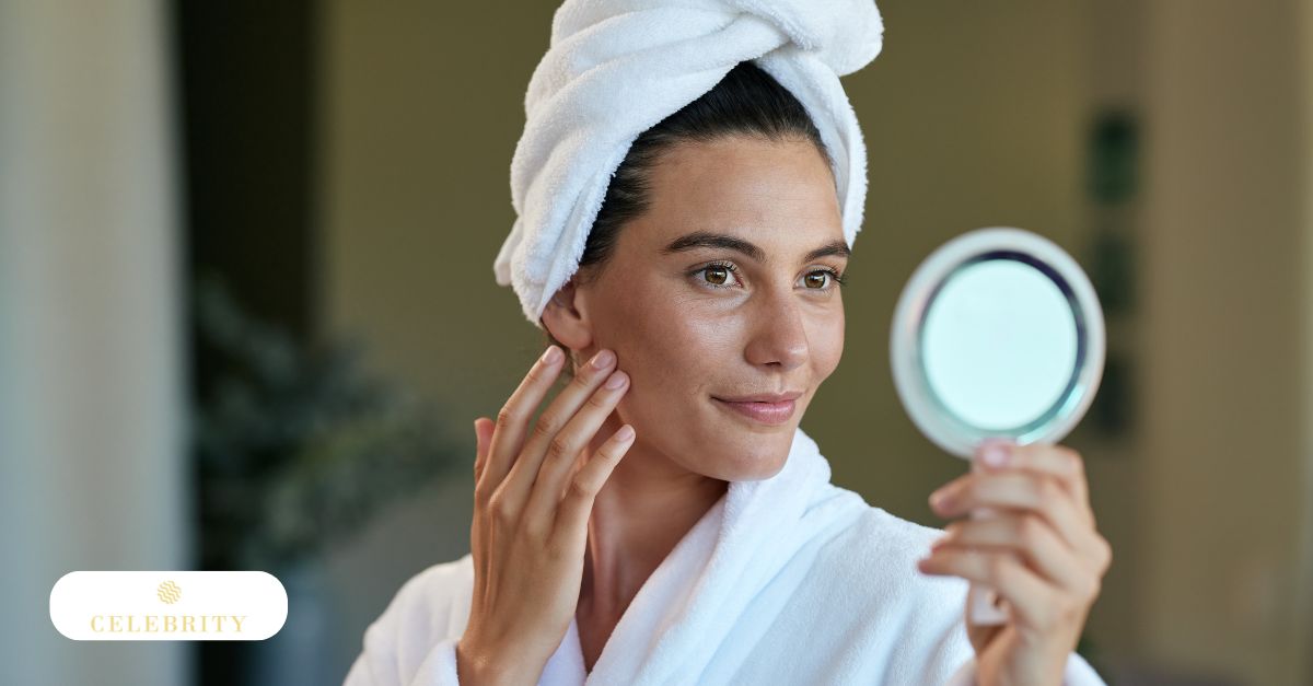 A woman in a white bathrobe looks into a small mirror and gently touches her smooth cheek to see when results appear after Morpheus8 following her skin treatment.