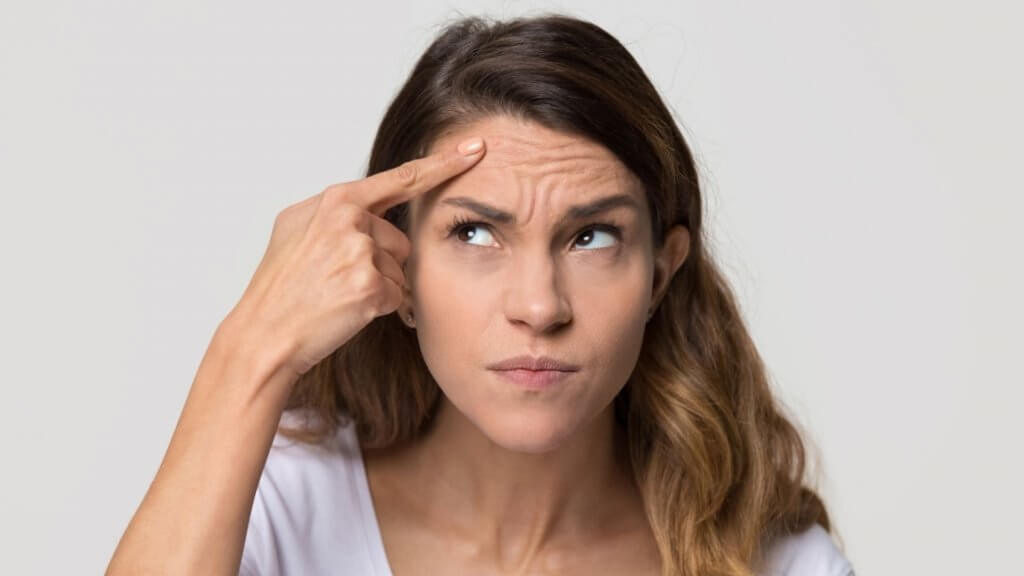 A depressed young woman touching forehead is worried about facial wrinkle