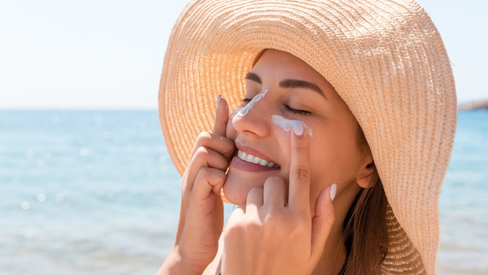 Smiling woman in hat is applying sunscreen