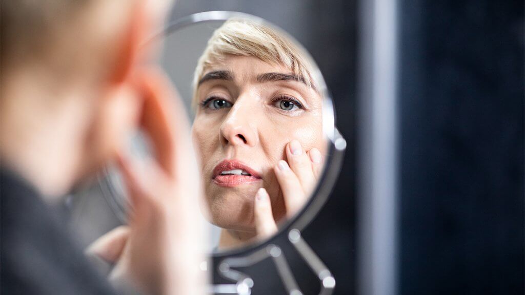 Middle-aged lady looking in mirror at wrinkles