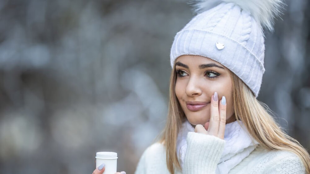 Beautiful girl applied face-cream on her cheek in winter