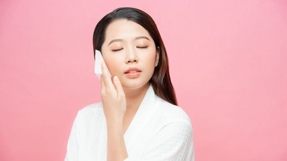 Face skin care and a woman using facial oil with blotting paper
