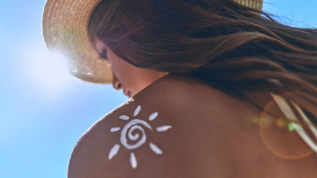 Woman with hat sitting under summer sun with sunscreen on her back