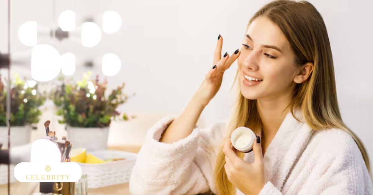A smiling woman gently applies cream to her face, with a clean lineup of cleanser, moisturizer, and sunscreen visible in the background