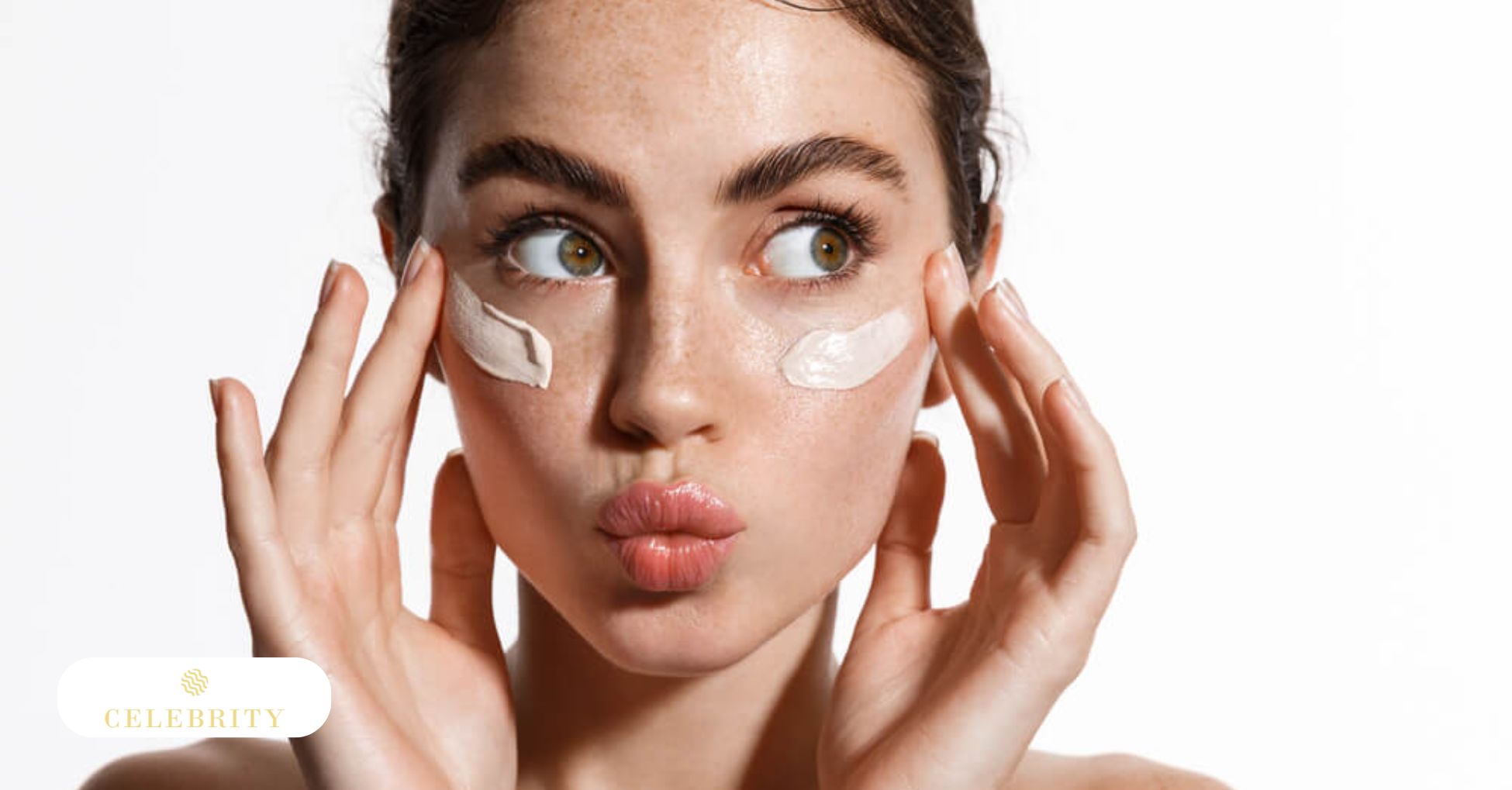 Woman with freckles applying two stripes of white skincare cream under her eyes while making a playful face